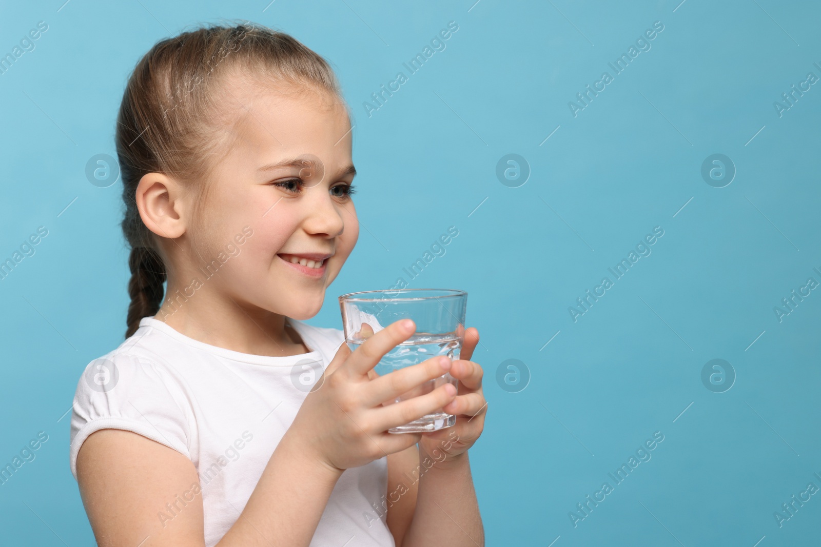 Photo of Happy little girl holding glass of fresh water on light blue background, space for text