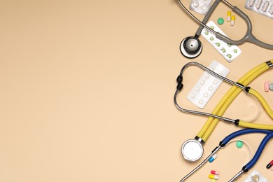 Stethoscopes and pills on beige background, flat lay. Space for text