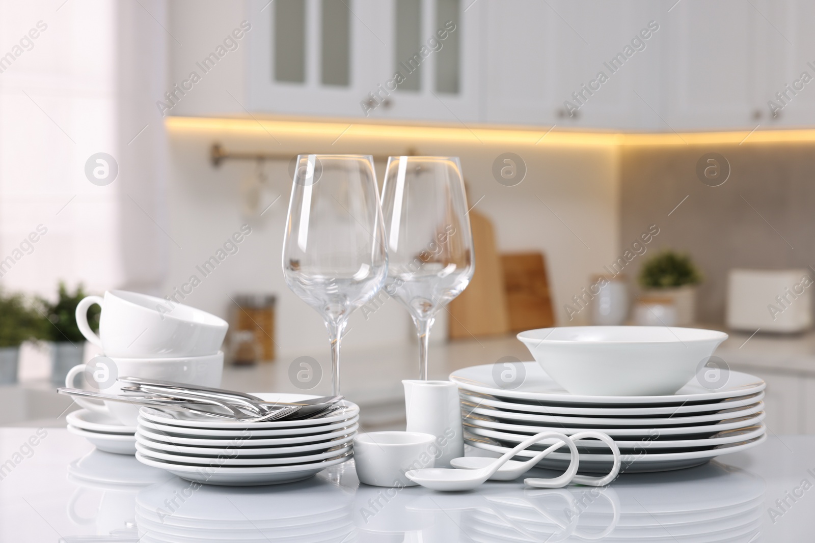 Photo of Set of clean dishware, glasses and cutlery on table in kitchen