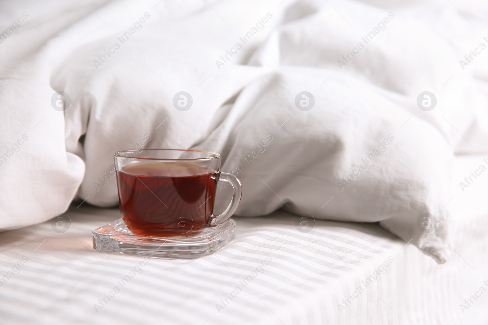 Photo of Glass cup with black tea near soft blanket on bed