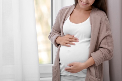 Photo of Pregnant woman standing near window at home, closeup