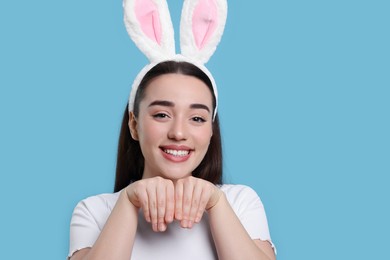Happy woman wearing bunny ears headband on turquoise background, space for text. Easter celebration