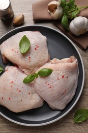 Photo of Raw chicken thighs with basil on wooden table, flat lay