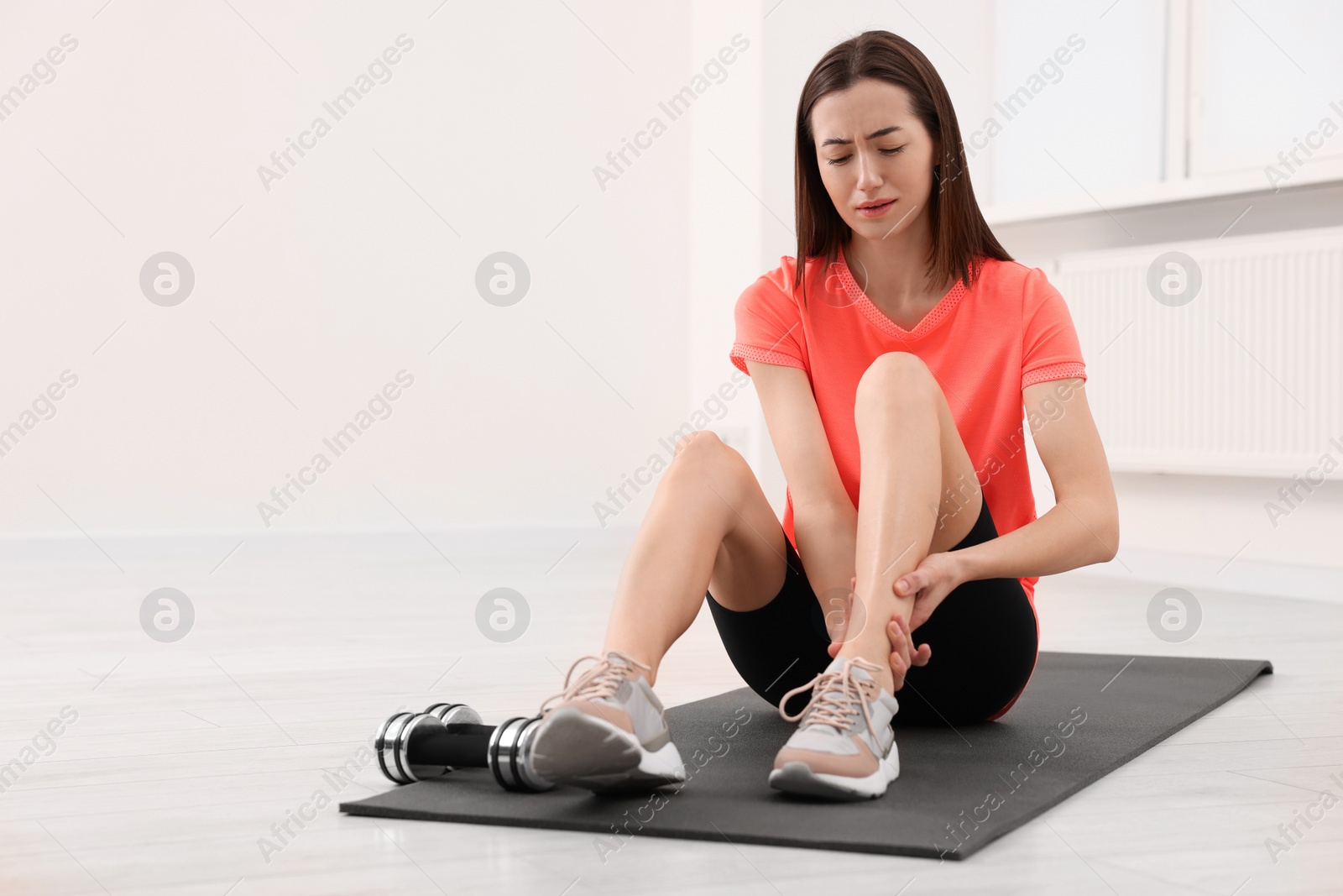 Photo of Young woman suffering from leg pain on exercise mat indoors, space for text