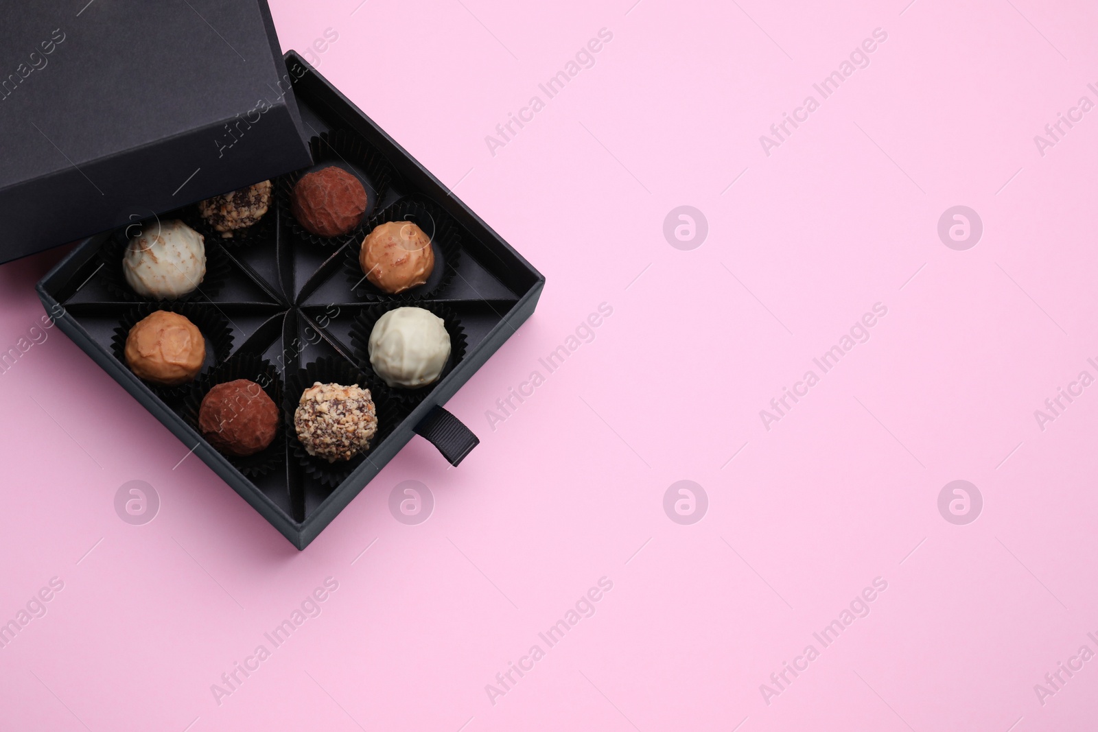 Photo of Box of tasty chocolate candies on pink background, top view. Space for text