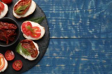 Photo of Delicious bruschettas with ricotta cheese, tomatoes, and dill on blue wooden table, top view. Space for text