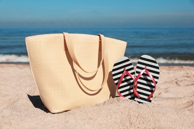 Photo of Striped flip flops and beach bag on sandy seashore