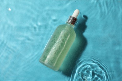Photo of Bottle of hydrophilic oil in water on light blue background, top view