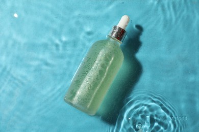 Bottle of hydrophilic oil in water on light blue background, top view