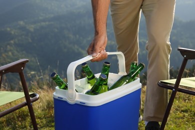 Man holding cool box with bottles of beer in nature, closeup