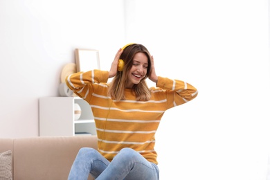 Photo of Young woman in headphones enjoying music on sofa at home