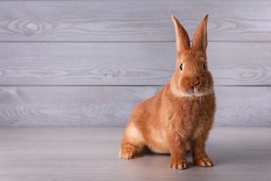 Photo of Cute bunny on grey table against wooden background, space for text. Easter symbol