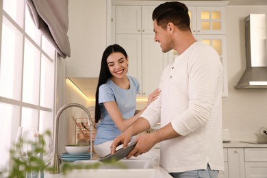 Photo of Happy lovely couple washing dishes in kitchen