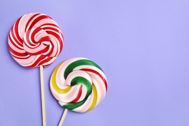 Sticks with colorful lollipops on violet background, flat lay. Space for text