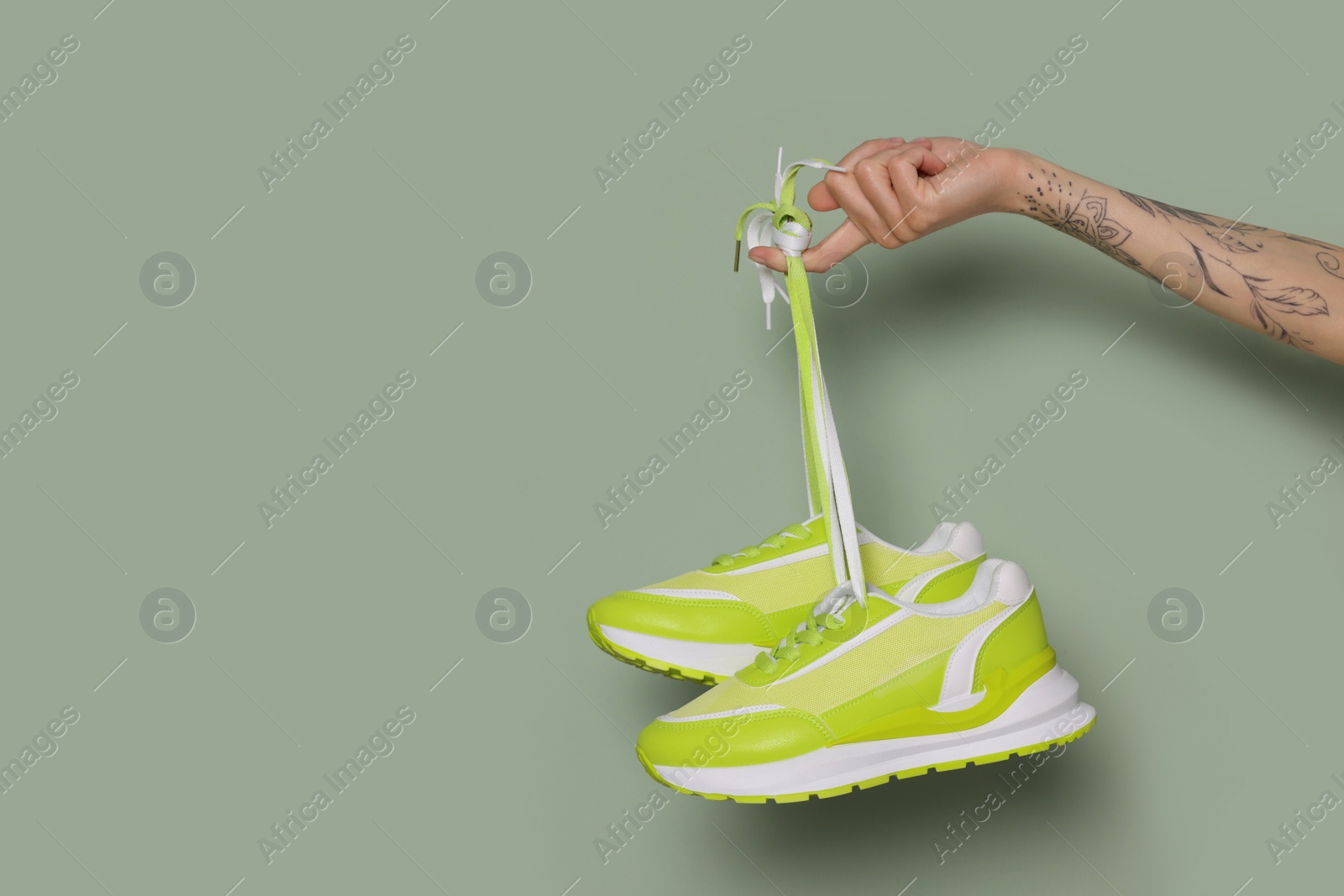 Photo of Woman holding pair of stylish sneakers on light green background, closeup. Space for text