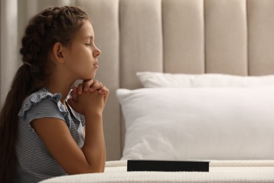 Photo of Cute little girl praying over Bible in bedroom. Space for text