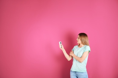 Woman with air conditioner remote on color background