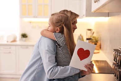 Photo of Little daughter congratulating her mom with greeting card in kitchen. Happy Mother's Day