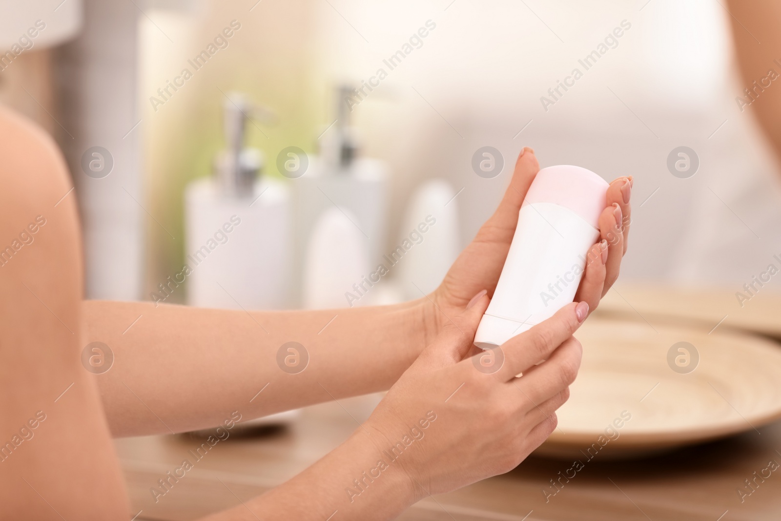 Photo of Young woman holding deodorant in bathroom, closeup