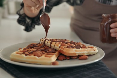 Woman decorating delicious Belgian waffles with chocolate cream at white countertop in kitchen, closeup