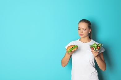 Photo of Young woman with salad and hamburger on color background. Healthy diet