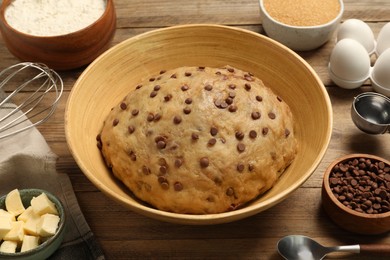 Photo of Fresh dough and ingredients for cooking chocolate chip cookies on wooden table, closeup