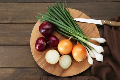 Photo of Board with different kinds of onions on wooden table, top view