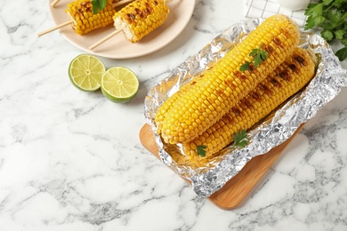 Tasty grilled corn on white marble table, flat lay