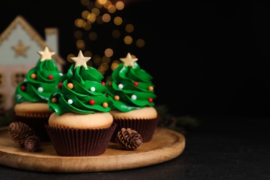 Photo of Christmas tree shaped cupcakes on black table. Space for text