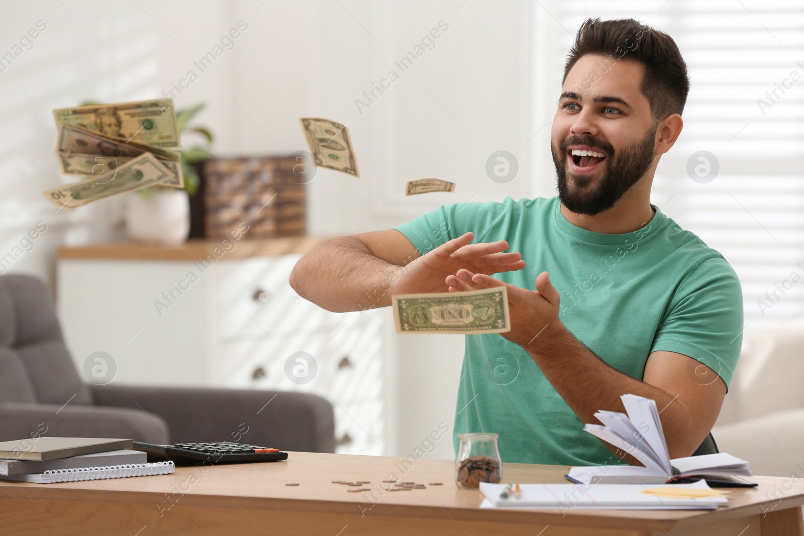 Photo of Happy young man throwing money at wooden table indoors