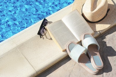 Photo of Stylish sunglasses, slippers, straw hat and book at poolside on sunny day. Beach accessories