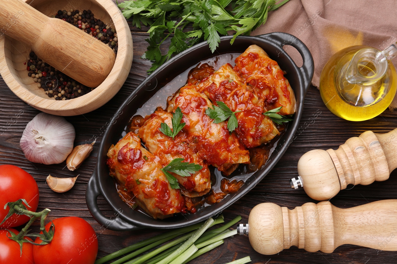 Photo of Delicious stuffed cabbage rolls cooked with tomato sauce and ingredients on wooden table, flat lay