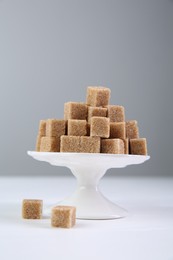 Photo of Brown sugar cubes on white table against light background