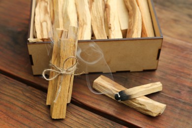 Many Palo Santo sticks and one smoldering on wooden table