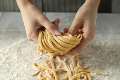 Woman with homemade pasta at light tiled table, closeup