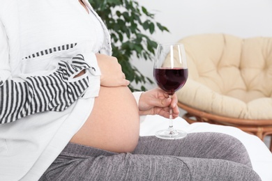 Photo of Pregnant woman with glass of red wine at home. Alcohol addiction