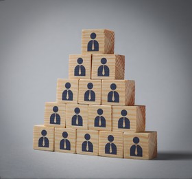 Image of Team and management concept. Pyramid of wooden cubes with human icons on grey background
