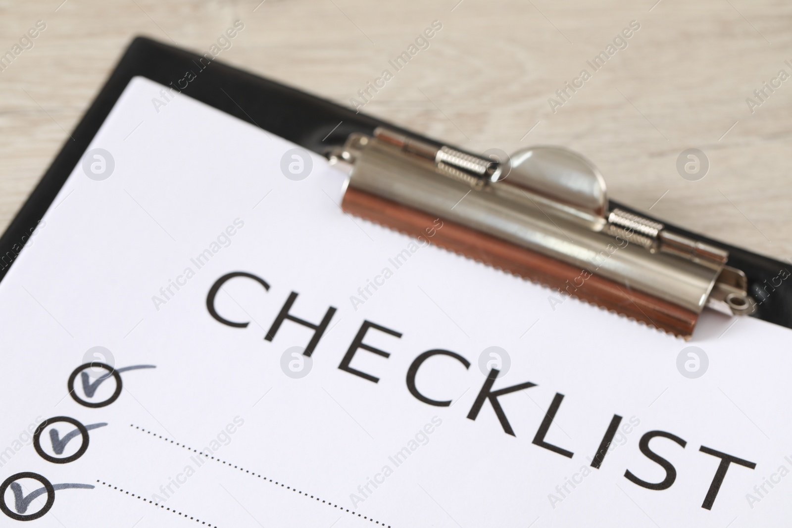 Photo of Clipboard with inscription Checklist on wooden table, closeup