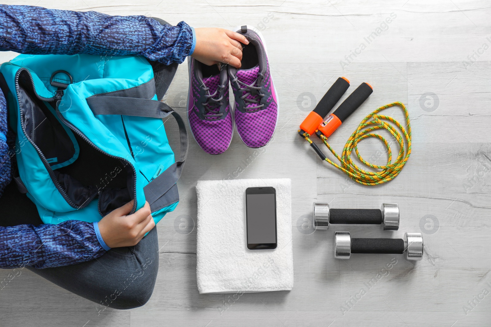 Photo of Young woman packing sports bag on floor, top view