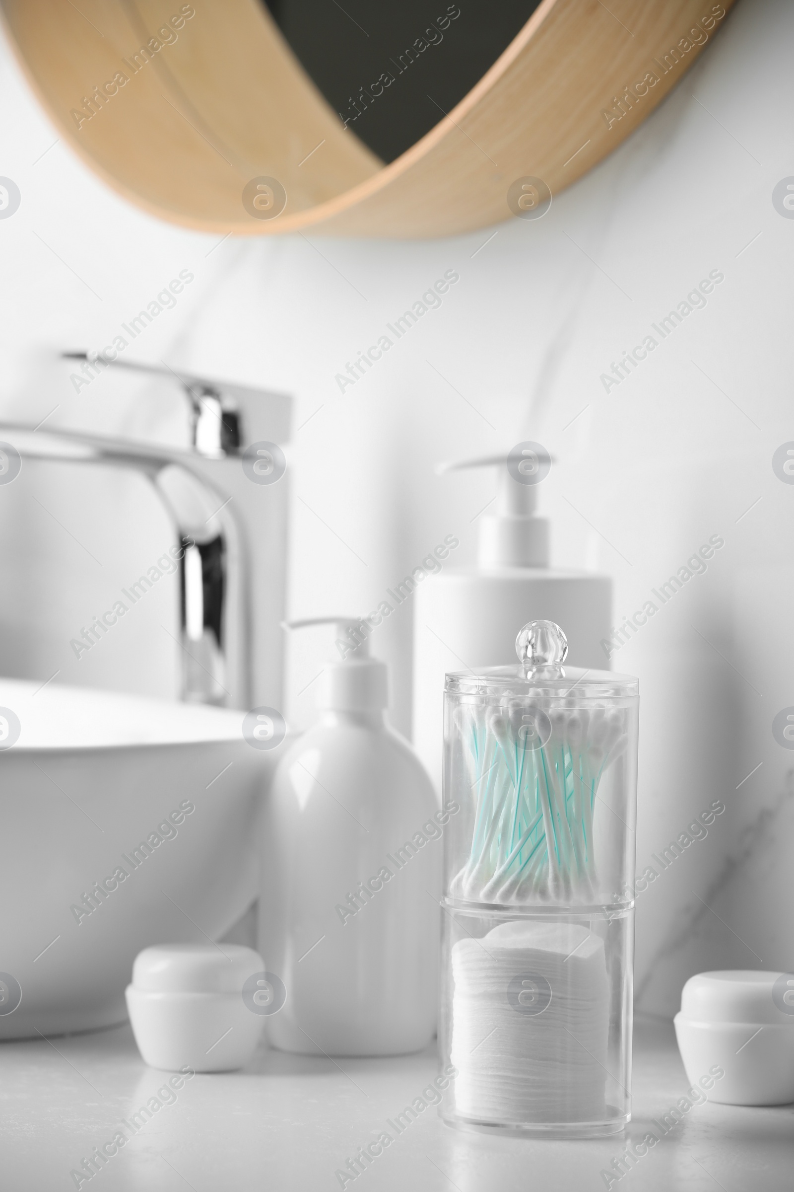 Photo of Containers with cotton swabs and pads near cosmetic products on white countertop in bathroom