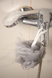 Grey shower puff hanging on faucet in bathroom, closeup