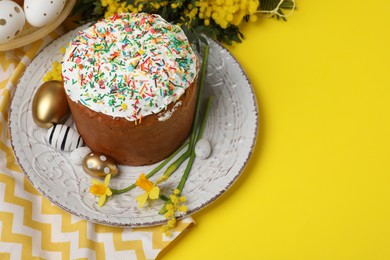 Photo of Traditional Easter cake with sprinkles, painted eggs and beautiful spring flowers on yellow background, space for text