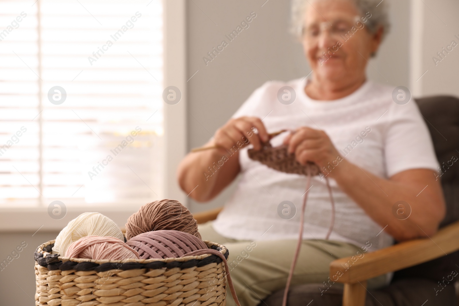Photo of Elderly woman knitting at home, focus on yarn. Creative hobby