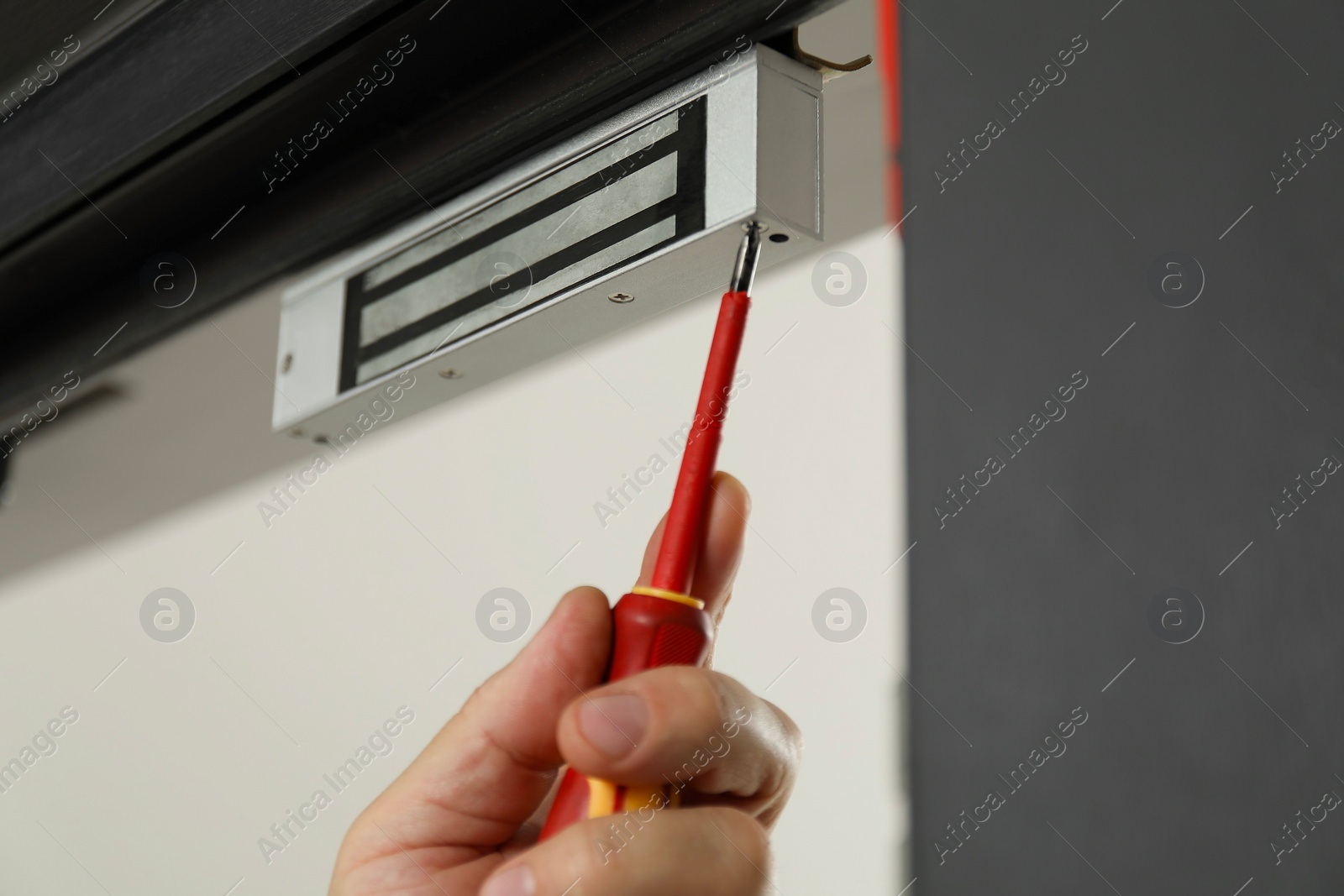 Photo of Man with screwdriver installing electromagnetic door lock indoors, closeup. Home security