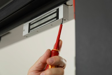 Man with screwdriver installing electromagnetic door lock indoors, closeup. Home security