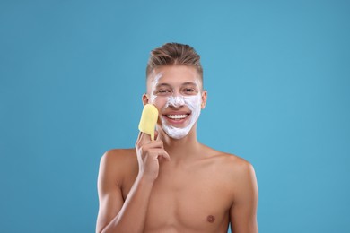 Photo of Happy young man washing off face mask with sponge on light blue background