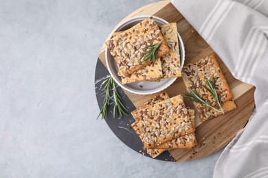 Photo of Cereal crackers with flax, sunflower, sesame seeds and rosemary on grey table, top view. Space for text