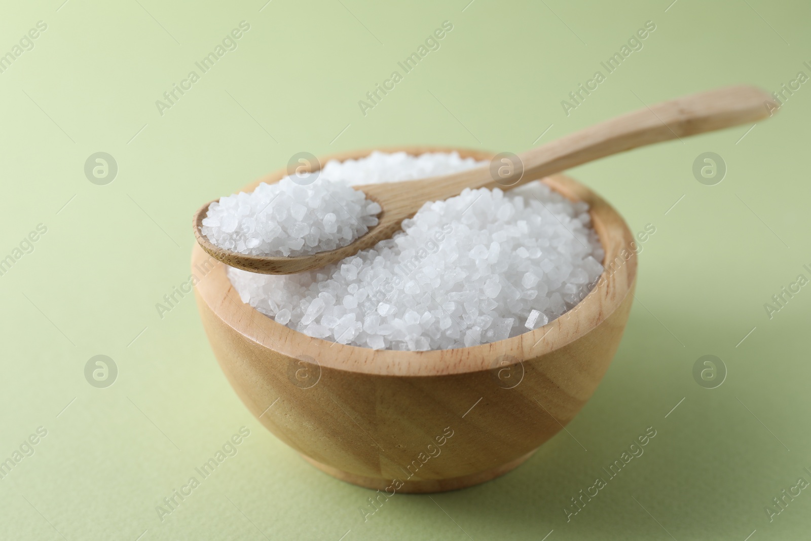 Photo of Organic white salt in bowl and spoon on olive background, closeup