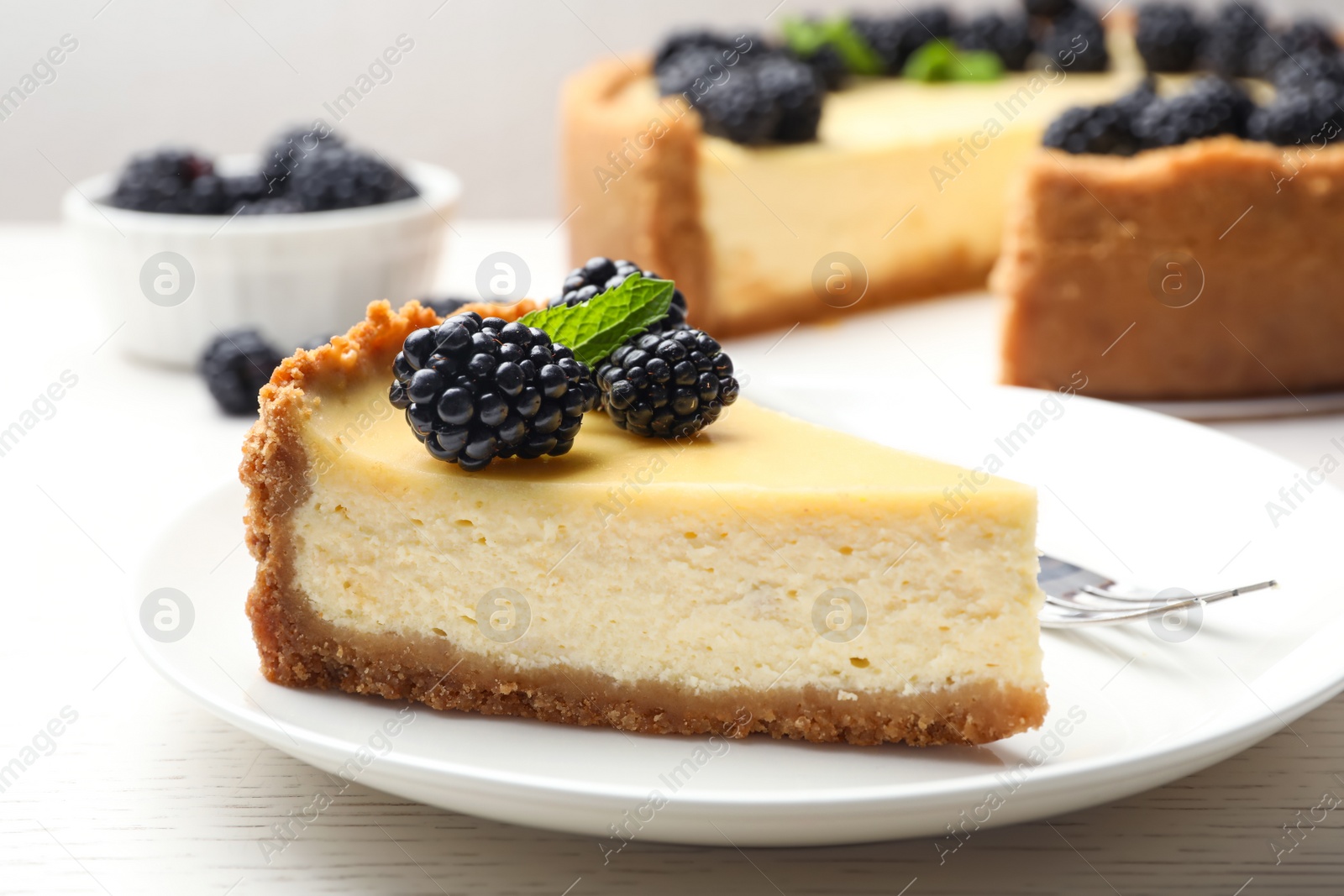 Photo of Piece of delicious cheesecake decorated with blackberries on table