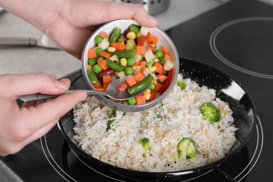 Photo of Woman cooking tasty rice with vegetables on induction stove, closeup